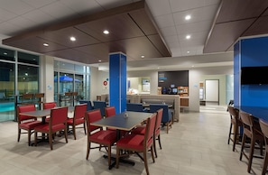 A modern dining area with red and blue seating, a pool view, and a coffee station. - Holiday Inn Express Lake Park by IHG (Lake Park)