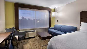 Una habitación de hotel con un ventanal grande, un sofá, una cama, un escritorio y una silla.
