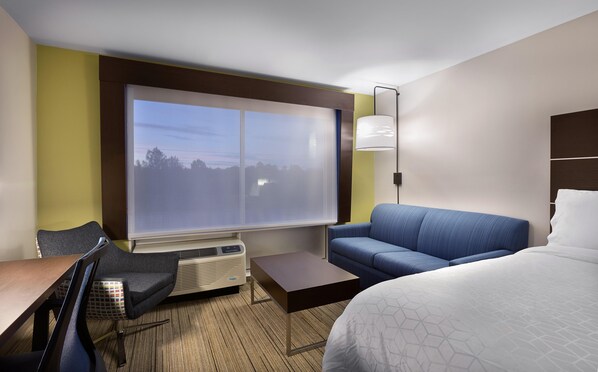 A hotel room with a large window, a sofa, a bed, a desk, and a chair. - Holiday Inn Express Lake Park by IHG (Lake Park)