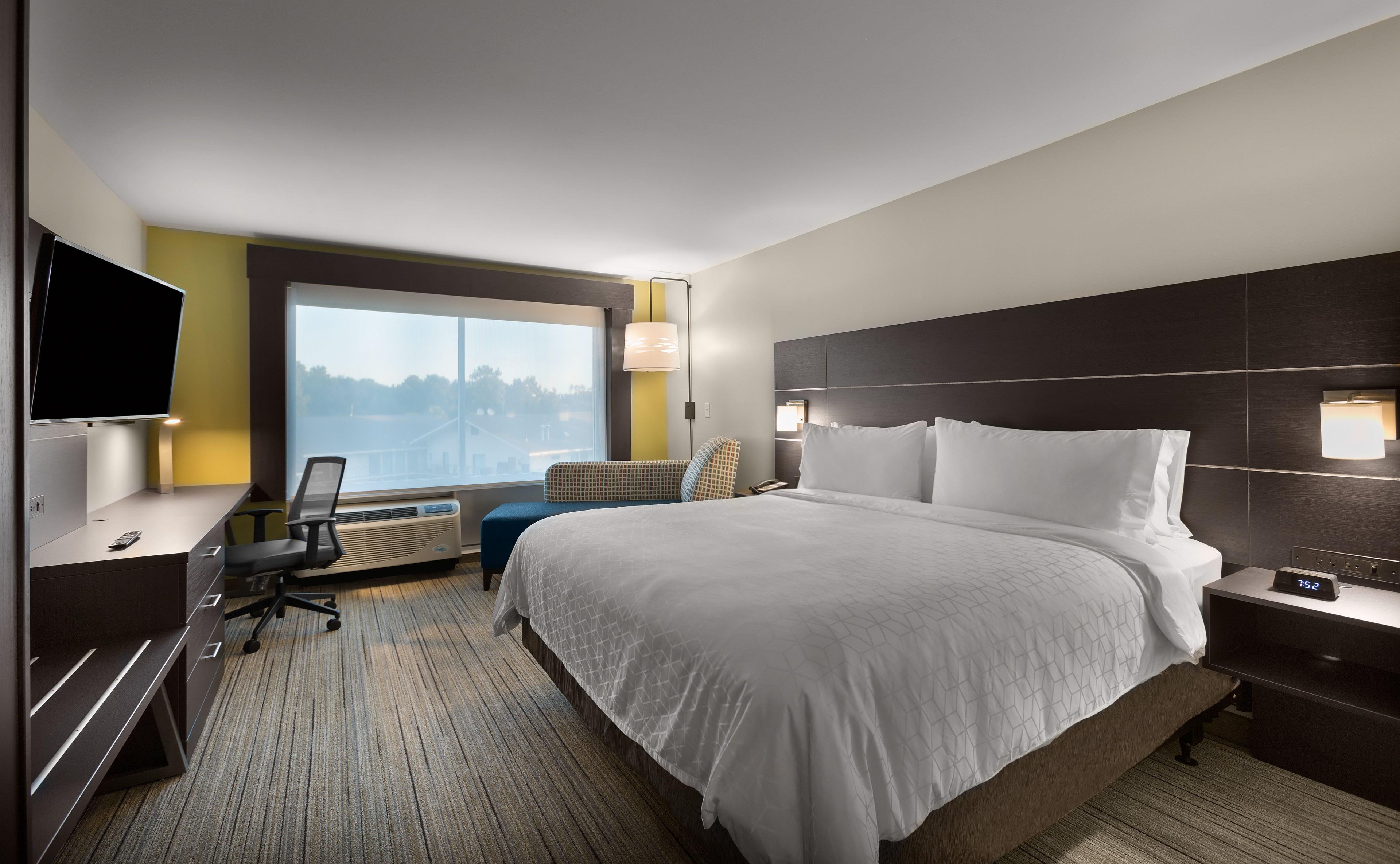 A hotel room with a large bed, a desk, a chair, a TV, and a window with a view.