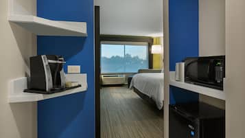 Hotelkamer met een bed, koffiezetapparaat, magnetron en uitzicht op bomen door een raam.