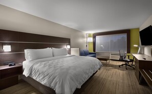 Une chambre d’hôtel avec un lit, une table de chevet, un bureau, une chaise et une grande fenêtre.