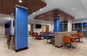 A modern dining area with blue and brown accents, multiple tables and chairs, and a television mounted on the wall. - Holiday Inn Express Lake Park by IHG (Lake Park)