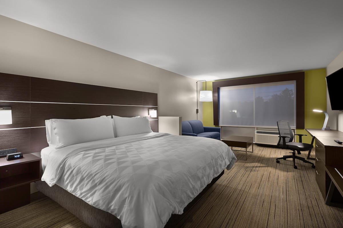 A hotel room with a large bed, bedside tables, a desk with a chair, a TV, and a window.