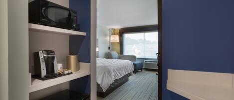 A hotel room with a bed, a microwave, a coffee maker, and a desk lamp.