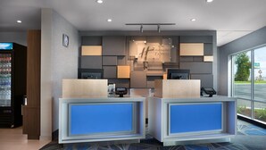 A Holiday Inn Express reception area with two reception counters, a clock on the wall, and a large window providing a view of the parking lot. - Holiday Inn Express Lake Park by IHG (Lake Park)
