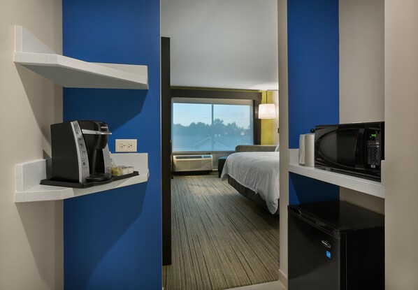 A hotel room with a bed, a coffee maker, a microwave, and a view of trees through a window. - Holiday Inn Express Lake Park by IHG (Lake Park)