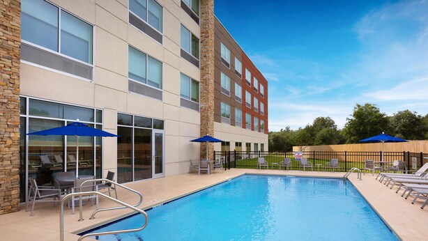 A swimming pool with lounge chairs and umbrellas, surrounded by a building with multiple windows and a stone facade. - Holiday Inn Express Lake Park by IHG (Lake Park)