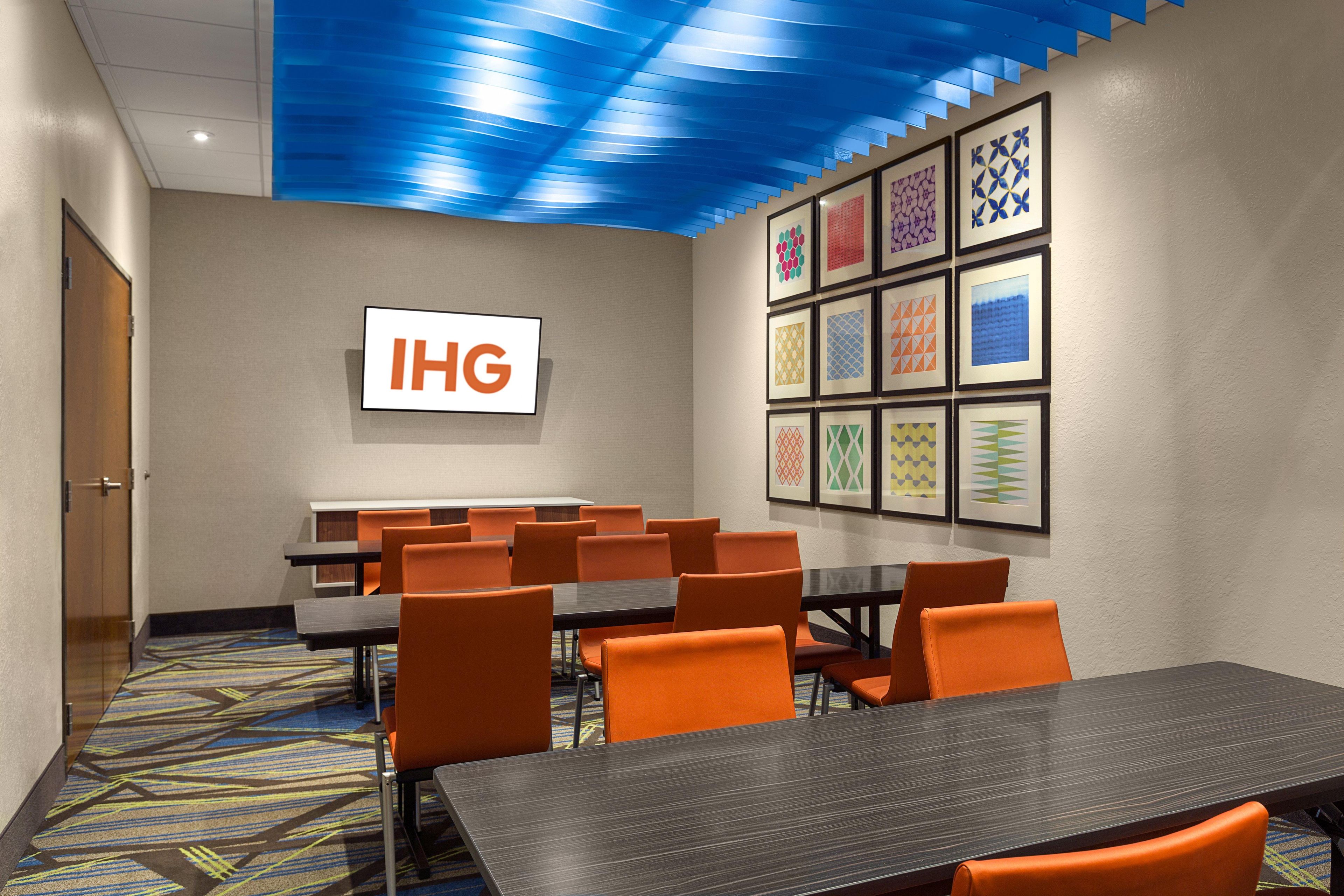 Un salón de conferencias con una gran mesa y varias sillas, un letrero con 'IHG' en la pared y una decoración con diseños en el techo.