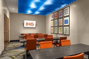 A conference room with a large table and multiple chairs, a sign with 'IHG' on the wall, and patterned artwork on the ceiling. - Holiday Inn Express Lake Park by IHG (Lake Park)