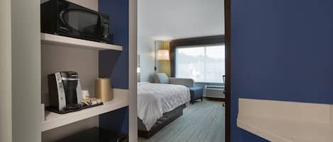 A hotel room with a bed, a microwave, a coffee maker, and a desk lamp.