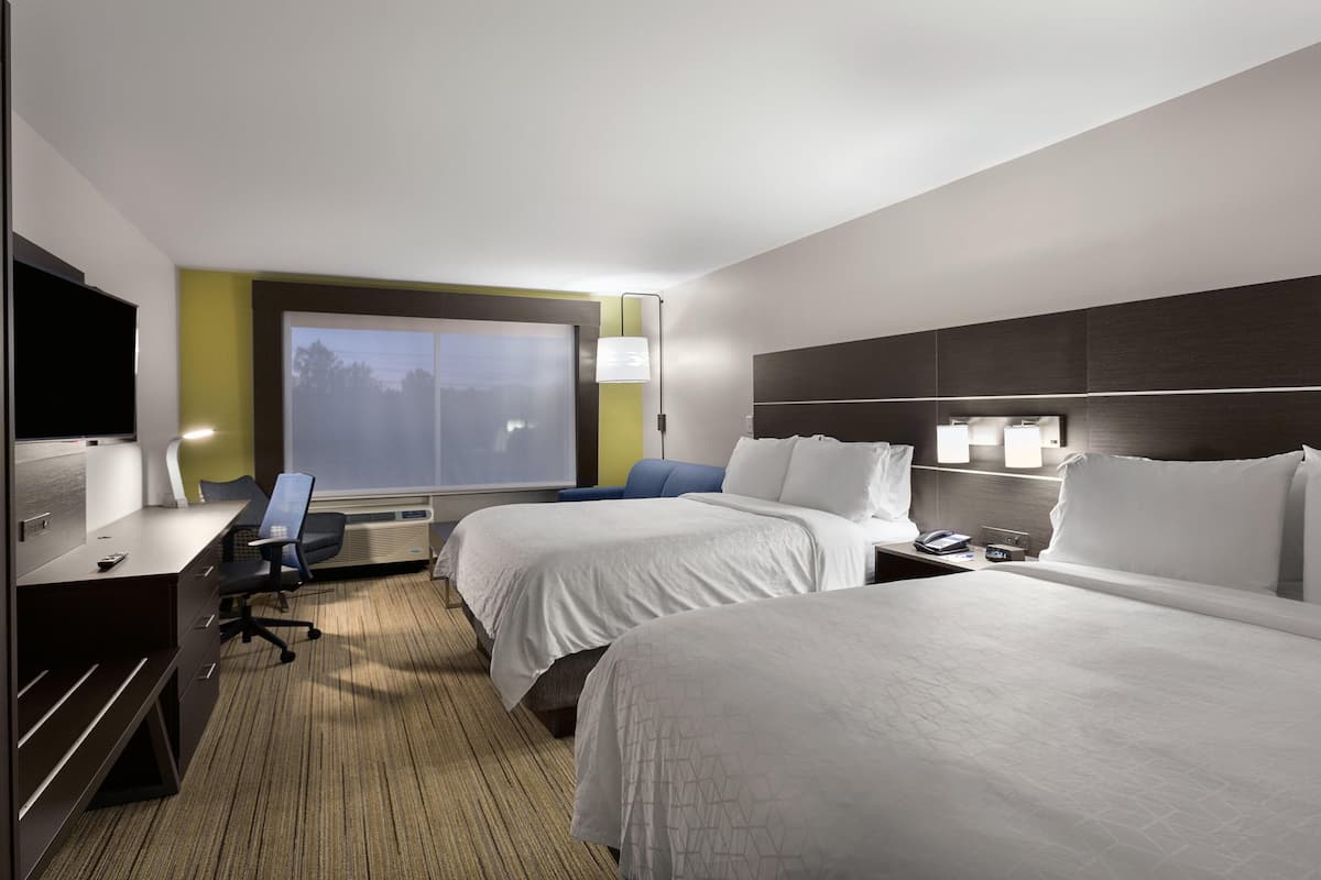 A hotel room with two beds, a desk, a chair, a TV, and a window.