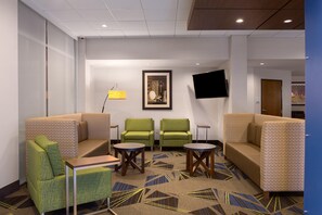 A hotel lobby with a sofa, two armchairs, a coffee table, a TV mounted on the wall, and a patterned carpet. - Holiday Inn Express Lake Park by IHG (Lake Park)