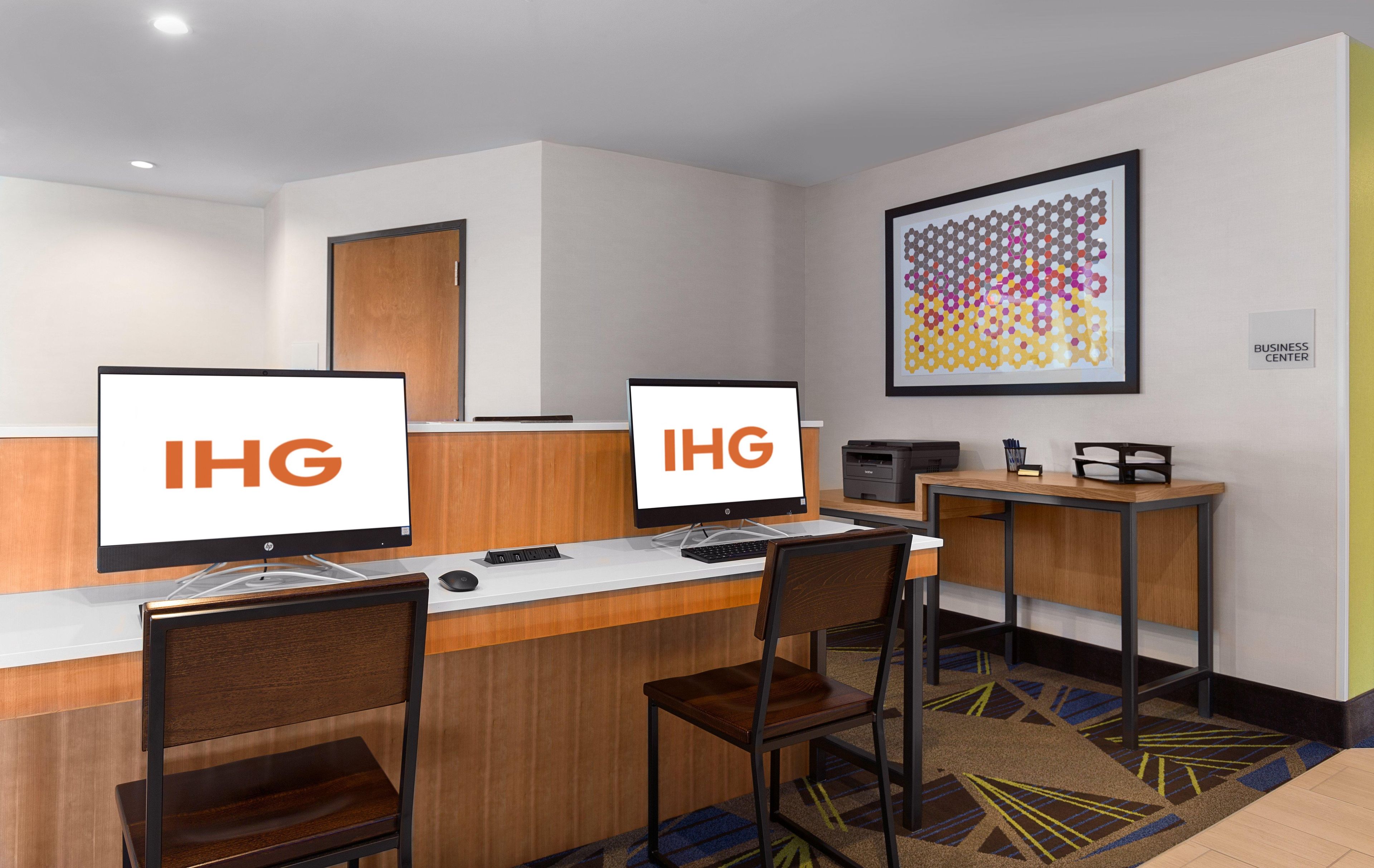 Een bedrijfsruimte met twee computerwerkstations, elk met het IHG-logo, een printer en een bureau met een stoel.