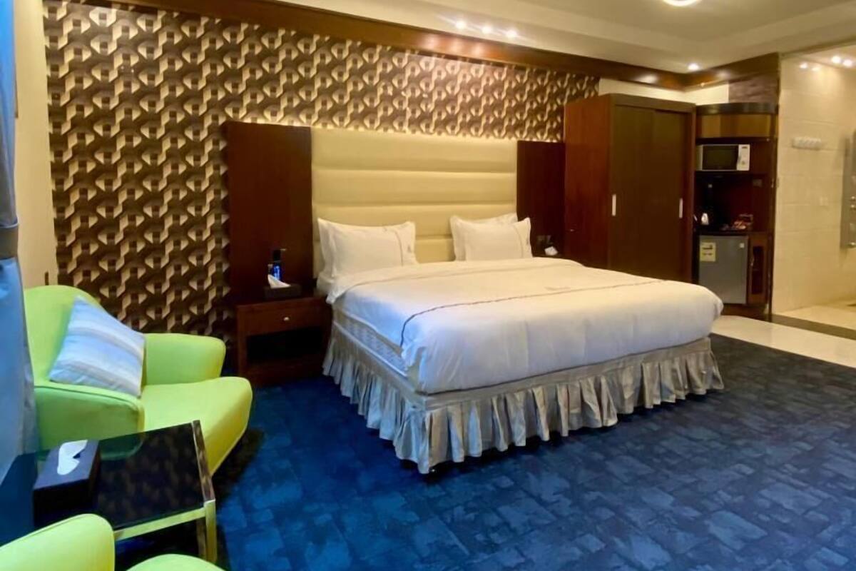 A hotel room with a large bed, a green sofa, a small table, and a patterned carpet.