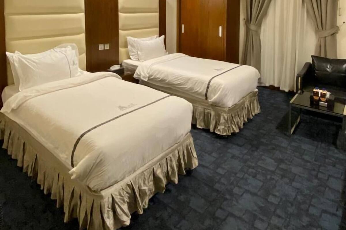 A hotel room with two beds, a desk, a chair, and a wardrobe.