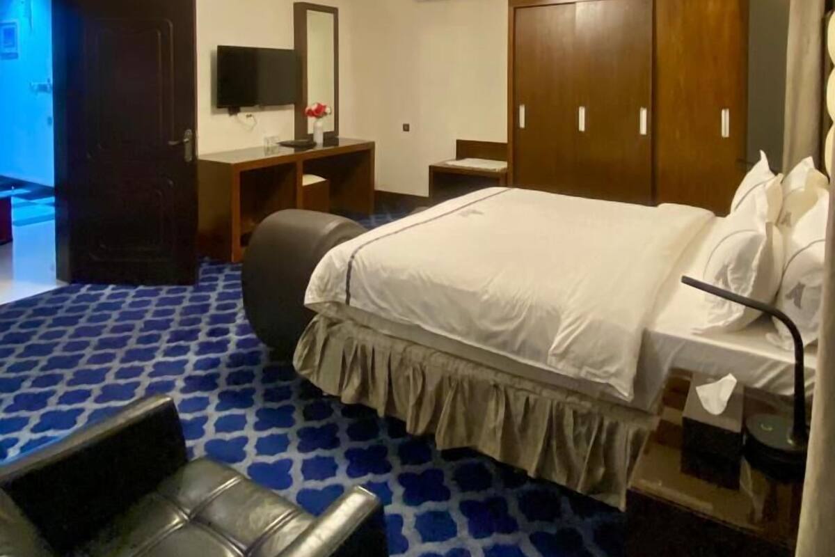A hotel room with a bed, a desk, a chair, a wardrobe, and an air conditioning unit.