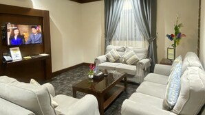 A living room with a flat-screen TV, two sofas, a coffee table, and a large window with curtains. - Aral Hotel (Tabuk)