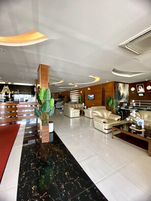 A modern lobby with a marble floor, leather sofas, a reception desk, and a large plant. - Aral Hotel (Tabuk)