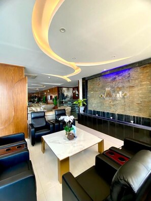 A modern hotel lobby with a marble coffee table, leather seating, a stone accent wall, and a reception area in the background. - Aral Hotel (Tabuk)