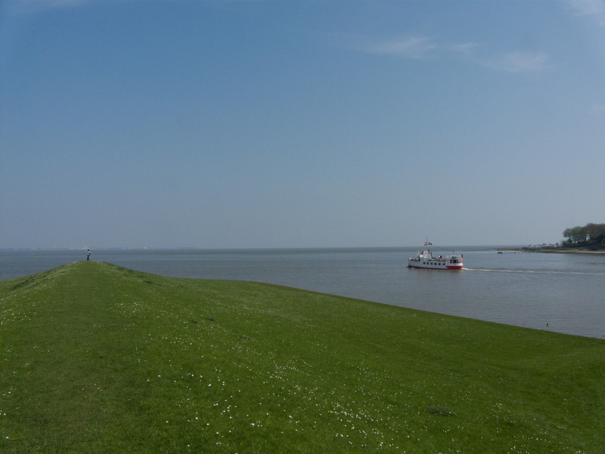 Ein grasbewachsener Hang, der zu einem Gewässer mit einem Boot in der Ferne führt.