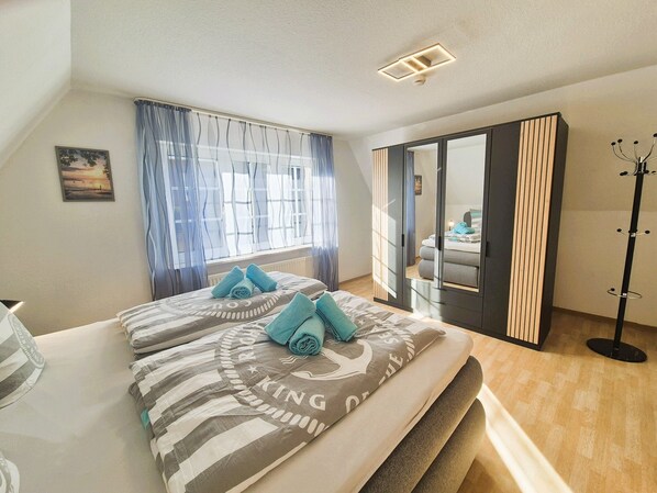 Ein Schlafzimmer mit einem Bett, einem fensterbelaubten Fenster, einem Spiegel und einem Kleiderständer.