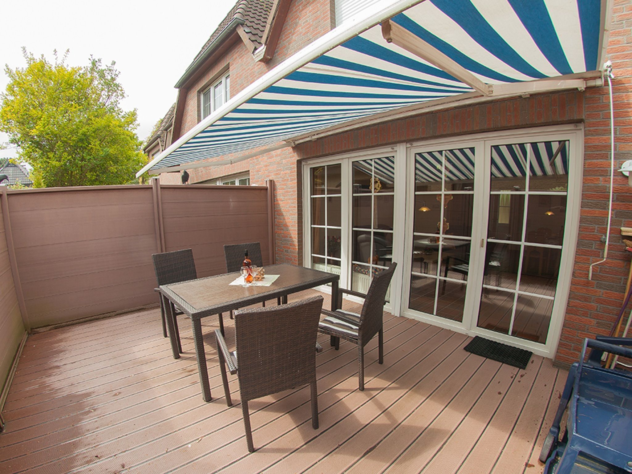 A patio with a table and chairs, a covered area with striped awning, and a brick wall.