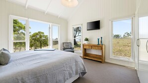 Ein Schlafzimmer mit einem großen Bett, einem an der Wand montierten Fernseher und Blick ins Freie durch die Fenster.