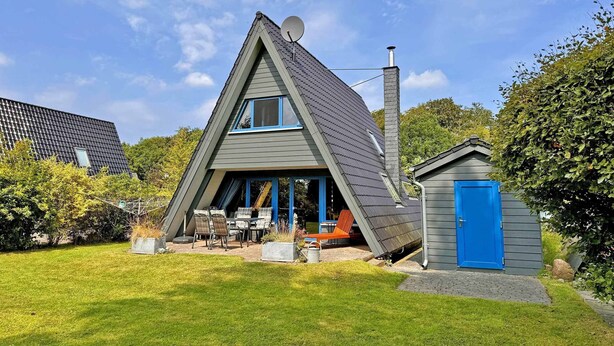 Une maison moderne de style A, dotée d’une antenne parabolique, d’une cheminée et d’un petit abri de jardin avec une porte bleue.