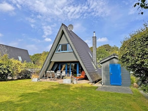 A modern A-frame house with a satellite dish, a chimney, and a small shed with a blue door.