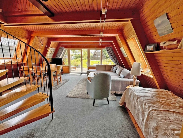 A cozy attic bedroom with a wooden staircase, a sofa, a chair, and a bed.