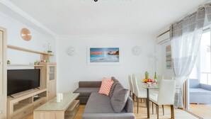 A modern living room with a flat-screen TV, grey sofa, and a dining area with a glass table and chairs.