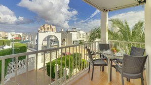 A balcony with a table set for dining, overlooking a cityscape with buildings and greenery.