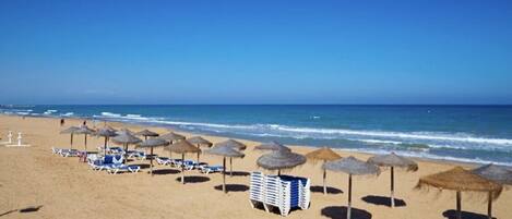 Una playa cerca, arena blanca, sillas reclinables de playa, sombrillas