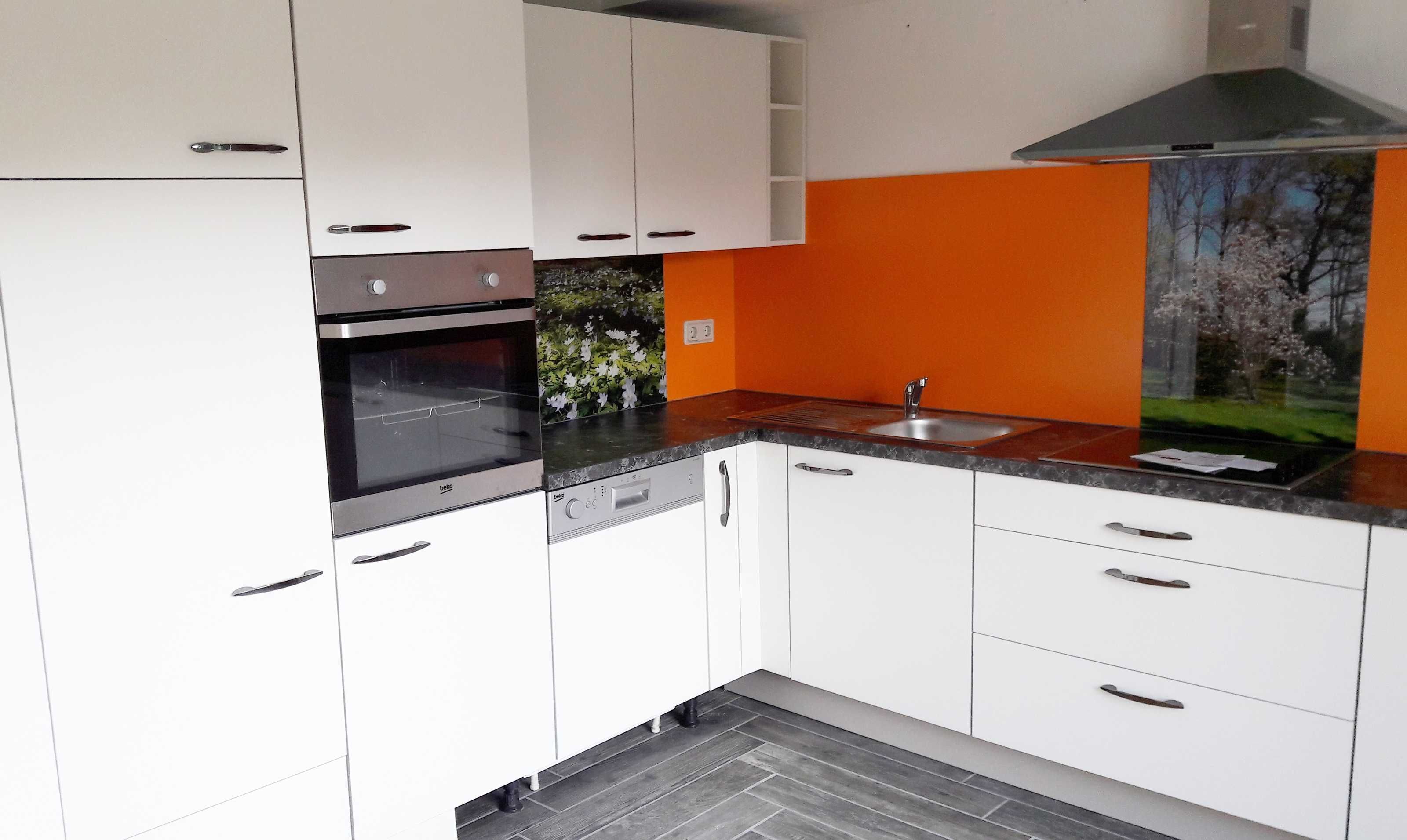 Una cocina moderna con gabinetes blancos, horno negro y salpicadero naranja.