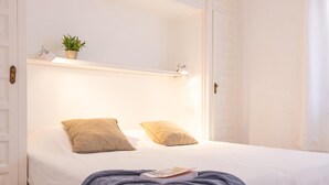 Une chambre à coucher avec un lit, deux oreillers, une table de chevet avec une plante et un livre posé sur le lit.