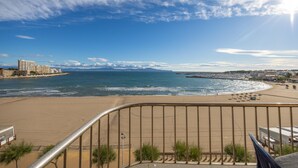 Une vue sur la plage, avec un ciel dégagé, une plage de sable et une silhouette de ville qui se dessine à l’horizon.