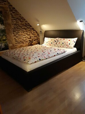 A bedroom with a stone wall, a bed with floral bedding, and a modern headboard.
