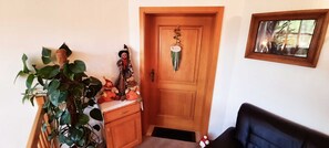 A wooden door, a plant, a small table with a decorative item, and a framed picture on the wall.