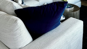 Een moderne woonkamer met een witte bank, blauw-witte kussens en een ronde salontafel.