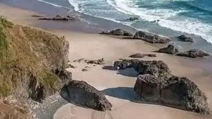 Een kuststrand met heldere lucht, rotsachtige uitstulpingen en een zandstrand.