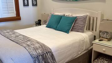 A bedroom with a bed, a nightstand, a lamp, a wall-mounted surfboard, and framed pictures.