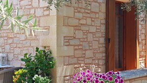Un mur de pierre avec une porte en bois, des plantes en pot fleuries et une chaise en osier.