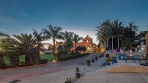 Un espacio exterior bien cuidado con piscina, palmeras y un edificio histórico con cúpula.