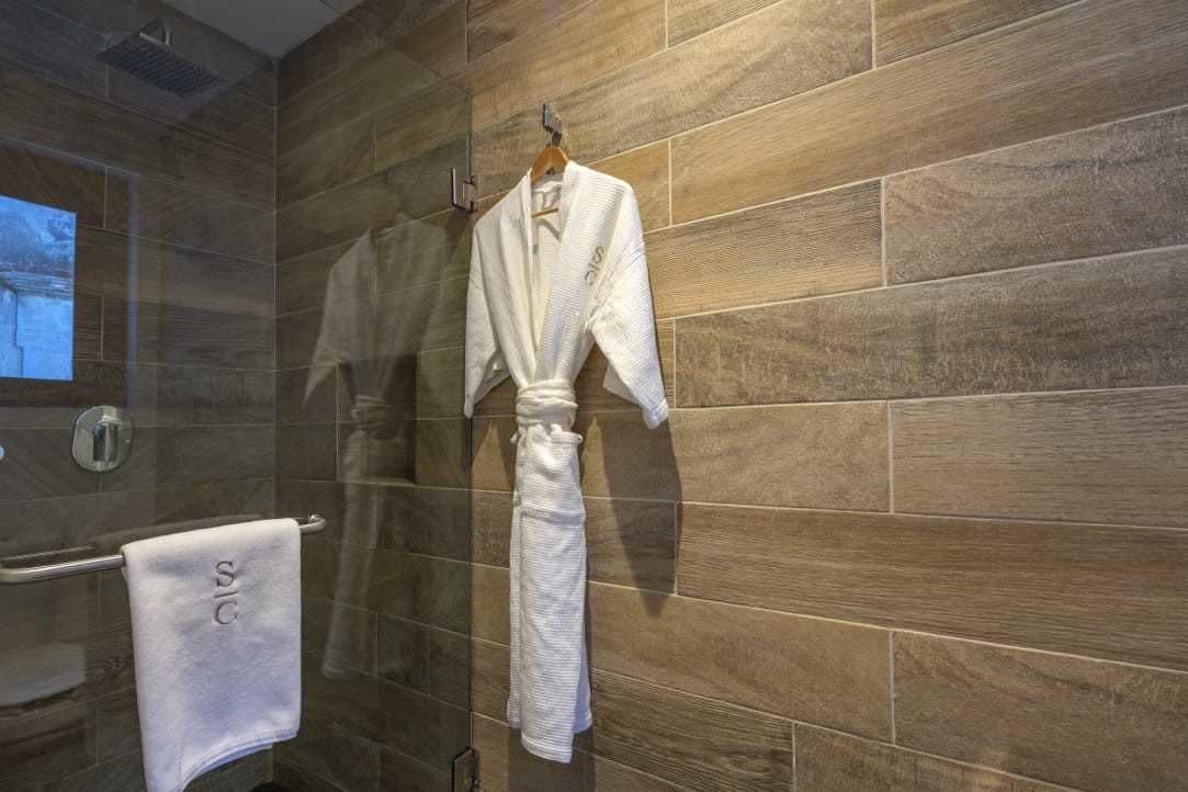 A bathroom with a wooden wall, a towel rack with a white towel, and a robe hanging on the rack.