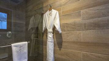 A bathroom with a wooden wall, a towel rack with a white towel, and a robe hanging on the rack.