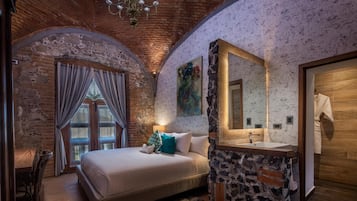 Camera da letto con un letto grande, una parete decorata in pietra, una porta in legno e un bagno con uno specchio ampio e un lavandino.