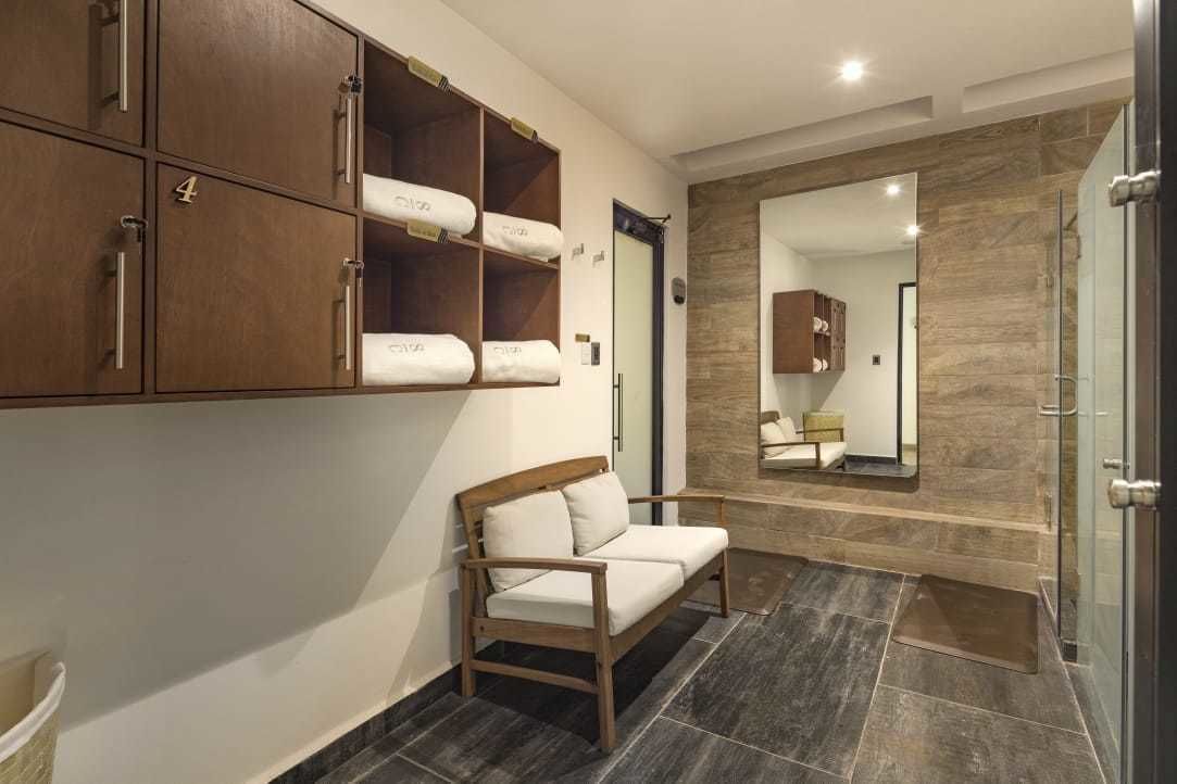 Habitación de hotel con un banco de madera, un espejo grande y un armario con toallas.