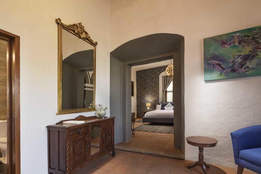A hallway with a large mirror, a wooden cabinet, a round table, and a blue chair.