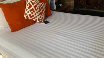 A neatly made bed with striped bedding and two pillows, a bedside lamp, and a wooden dresser in a room with stone walls and a fireplace.